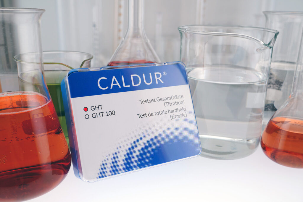 CALDUR® Testset Gesamthärte (Titration) zwischen Laborbechern und Kolben mit eingefärbten Lösungen